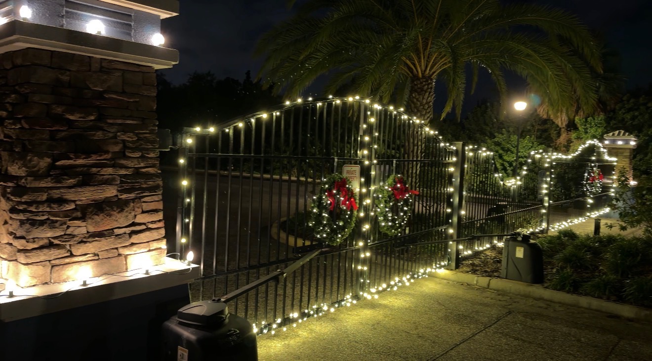 Front gate and fence wrapped in warm white lights with lit wreaths at a Palm Harbor home
