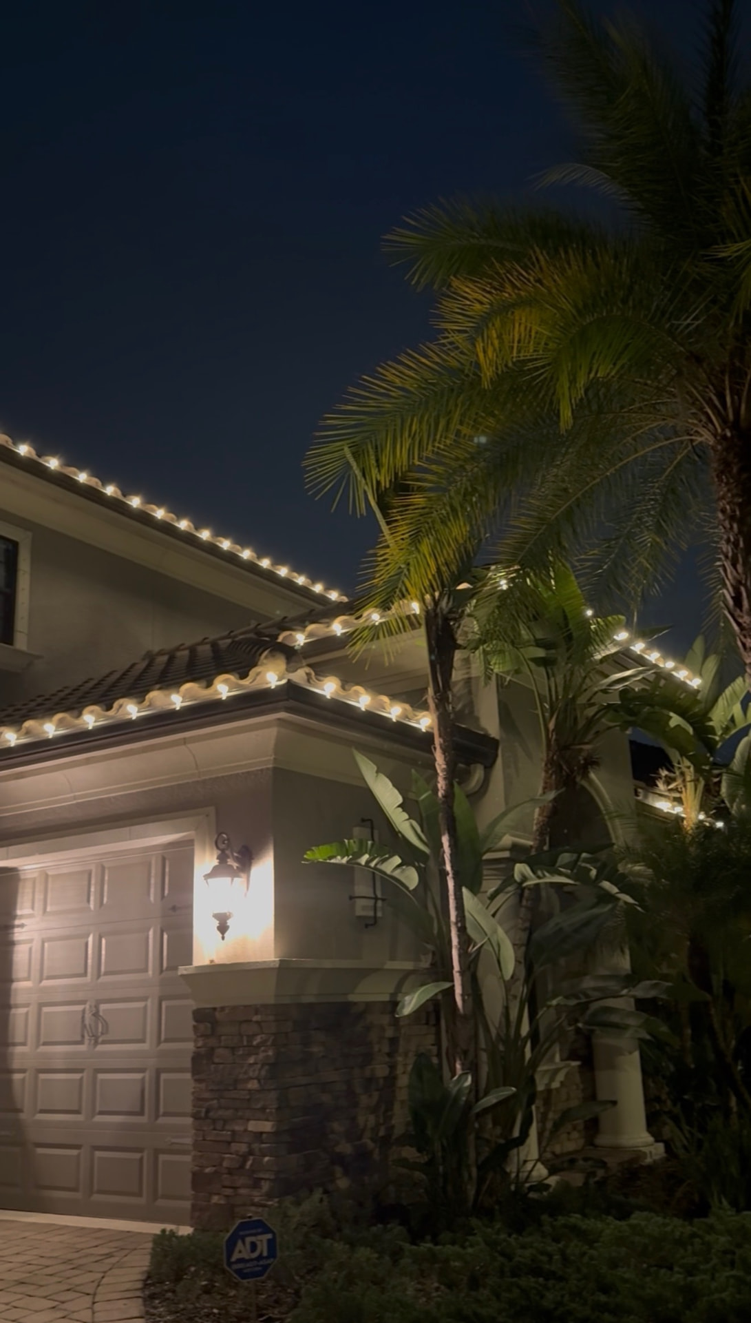 Garage roofline in warm white C9 lights with palms at night
