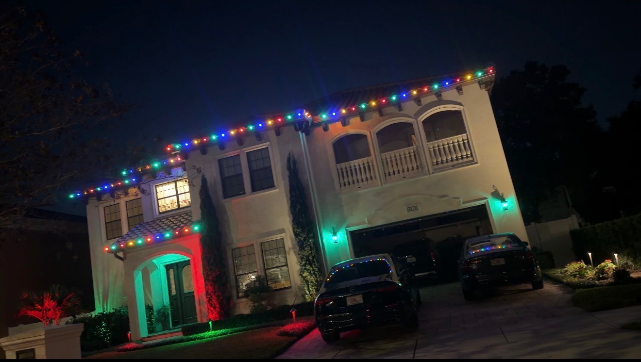 Two-story Tampa Bay area home with multicolor roofline lights and red and green landscape accents